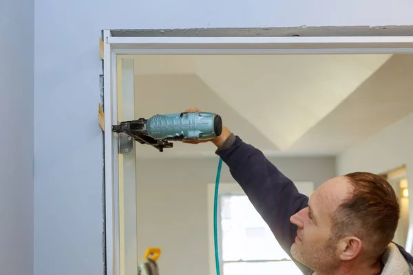 Manitas de construcción con pistola de clavos de aire instalando la puerta interior del apartamento —  Fotos de Stock