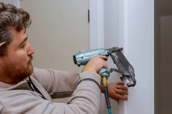 Manitas de construcción con pistola de clavos de aire instalando la puerta interior del apartamento — Foto de Stock