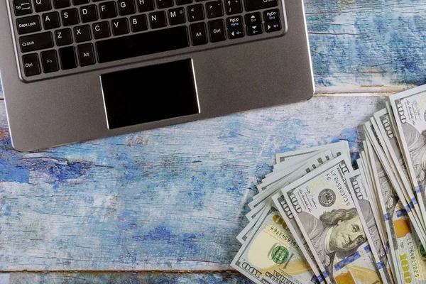 O dinheiro está ao lado do laptop na mesa de madeira azul . — Fotografia de Stock