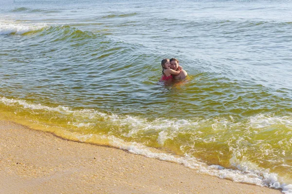 Menino segura menina em seus braços nas ondas do oceano . — Fotografia de Stock