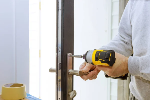 Installera dörrhandtaget med lås, snickare åt skruven, med hjälp av en borrmaskin, — Stockfoto