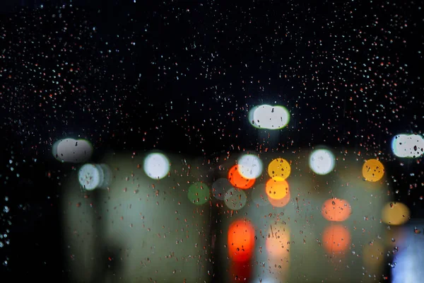 Blurred city street with waterdrops, neon lights and car — Stock Photo, Image