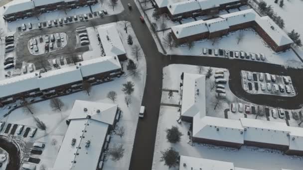 Dron aéreo volando bajo sobre una pequeña ciudad mientras casas y calles están cubiertas de nieve . — Vídeo de stock