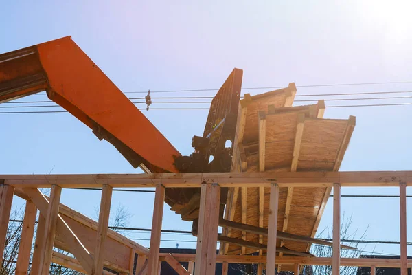 A wooden roof truss being lifted by a boom truck forklift in the roof of a new home