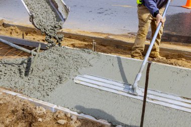 İnşaat işçisi inşaat alanında el arabası ve çimento ve çakıl döken karıştırıcı kamyonla beton işlerinde kaldırım için çimento döküyor.