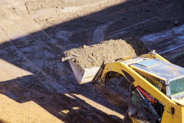 Buldozer hareket ediyor, yerdeki inşaat alanında kürekleri kullanarak zemini düzleştiriyor.