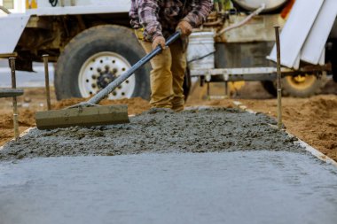 İnşaat işçisi inşaat alanında el arabası ve çimento ve çakıl döken karıştırıcı kamyonla beton işlerinde kaldırım için çimento döküyor.