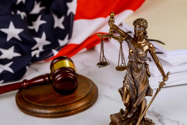 Figure of Justice holding the scales of justice with gavel on a law paper documents in against blurred USA flag