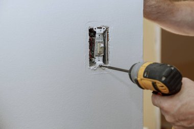 Eski şalterin yenisiyle değiştirilmesi, elektrikçinin duvar prizine yakın plan yerleştirmesi.