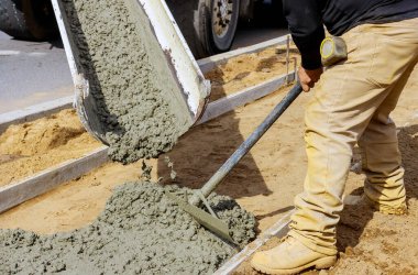 İnşaat işçisi inşaat alanında el arabası ve çimento ve çakıl döken karıştırıcı kamyonla beton işlerinde kaldırım için çimento döküyor.