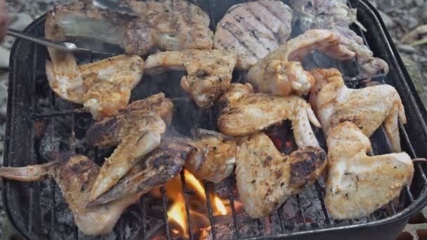 Запеченные куриные крылышки на дымящемся огне в переносном барбекю замедленной съемки — стоковое видео