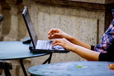 Kız dışarıda masada otururken iş için dizüstü bilgisayar kullanıyor.