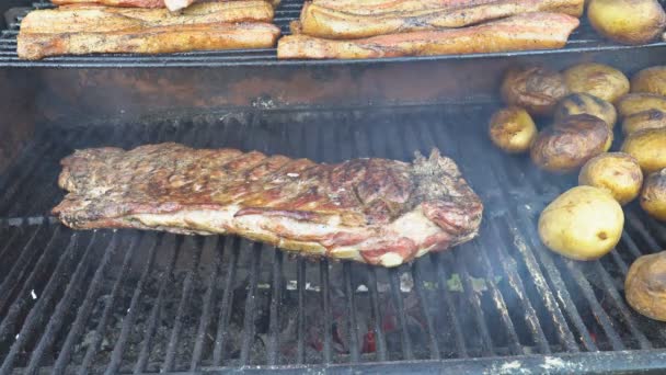 Ribs on barbecue grill with potatoes bacon slice cooking on barbecue grill — Stock Video