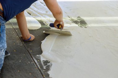 Bir inşaat işçisi zemini döşemek için beton zemine havan topluyor..