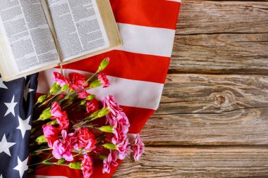 Los Angeles CA US 16 MAY 2020: Carnation flowers on Open reading Holy Bible on a close up of america pray in the American flag clipart