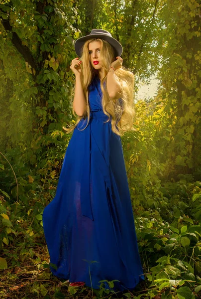 L fille avec les cheveux longs dans un chapeau et robe bleue posant en automne f — Photo