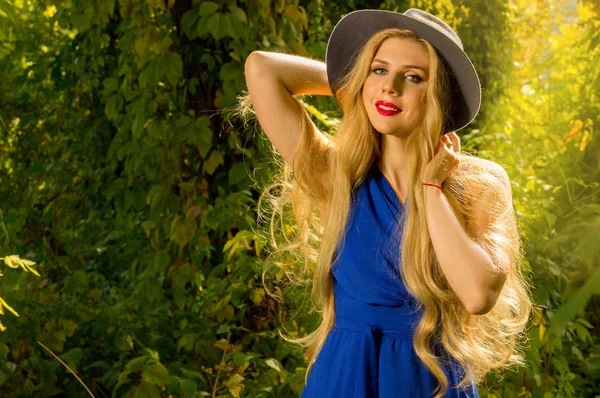 Девушка с длинными волосами в шляпе и синим платьем позирует осенью — стоковое фото