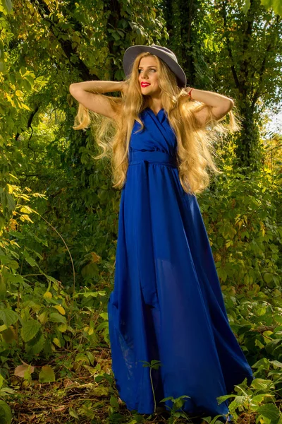 Girl with long hair in a hat and blue dress posing in autumn fo — Stock Photo, Image