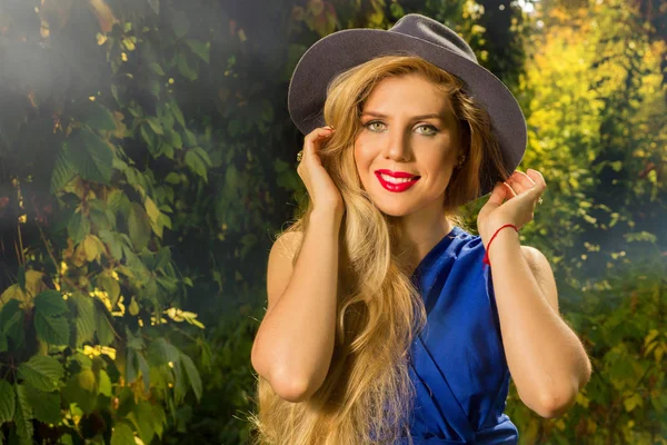 Hermosa chica con el pelo largo en un sombrero y vestido azul en un respaldo — Foto de Stock