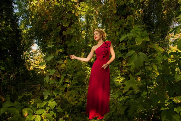 Beautiful girl in red dress posing on a background of  leaves — Stock Photo, Image