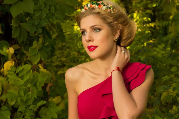 Schöne Mädchen in rotem Kleid posiert auf einem Hintergrund aus Blättern — Stockfoto