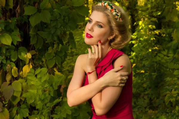 Menina bonita em vestido vermelho posando em um fundo de folhas — Fotografia de Stock