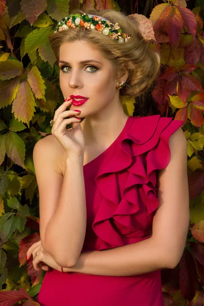 Mooi meisje in een rode jurk poseren op een achtergrond van bladeren — Stockfoto