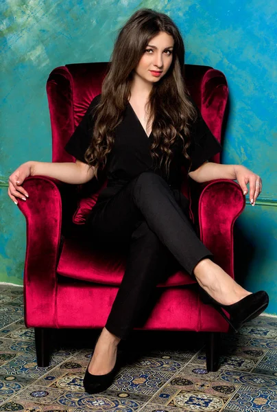 Schönes Mädchen im schwarzen Hosenanzug sitzt auf einem roten Stuhl — Stockfoto