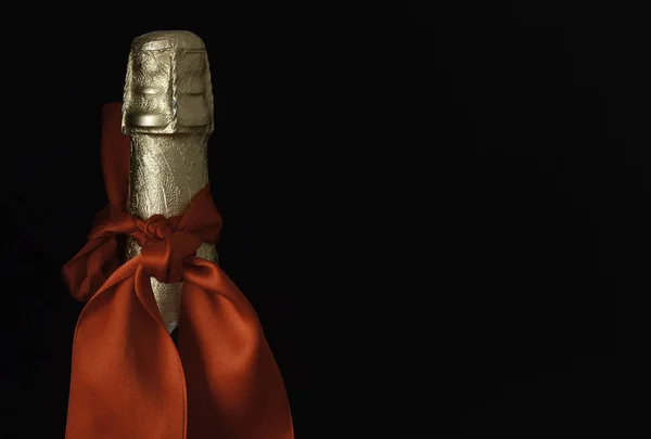 BOTTLE OF CHAMPAGNE WITH RED BOW ON BLACK BACKGROUND. CELEBRATION OF HOLIDAYS AND CHRISTMAS