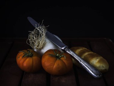 Tahta masada soğanlı, ekmekli ve metal bıçaklı kırmızı domatesler ve siyah arka plan.