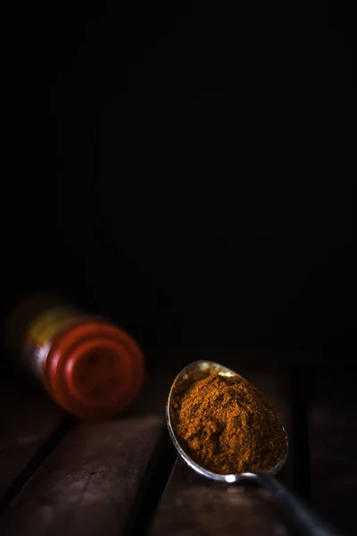 Rode peper in metalen lepel en kruidenpot op houten tafel en donkere achtergrond — Stockfoto