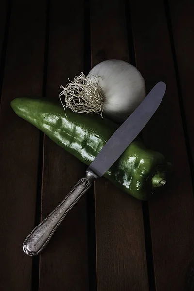 GREEN PEPPER AND ONION WITH ANTIQUE KNIFE ON WOODEN TABLE