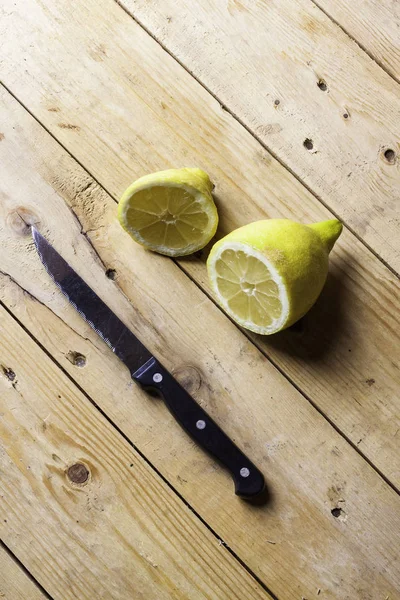 YELLOW LEMONS CUT WITH KITCHEN KNIFE ON WOODEN TABLE. RUSTIC FOOD PHOTOGRAPHY