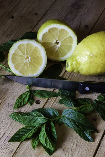 YELLOW LEMON CUT WITH KITCHEN KNIFE ON WOODEN TABLE AND AROMATIC LEAVES