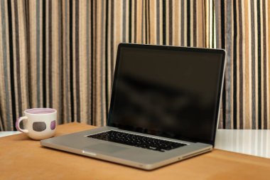 Ofisteki masada siyah ekranlı dizüstü bilgisayar ve kahve fincanı.