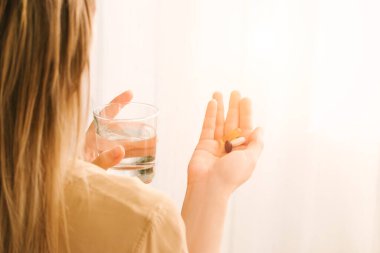 Kadın vitamin alır ve bir bardak su tutar..
