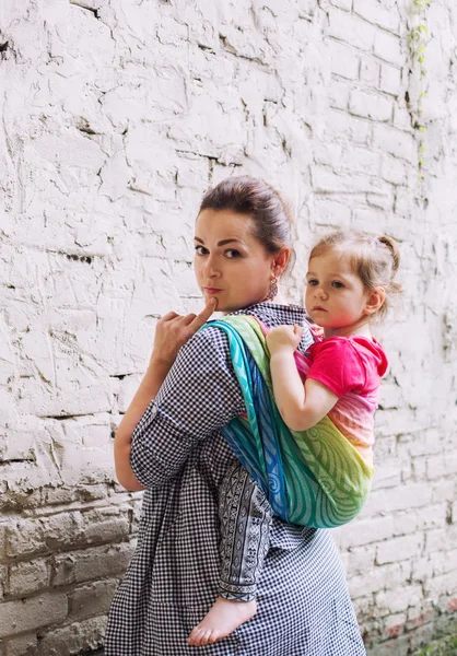 母と幼児の娘の家族は ラップベビーキャリアスリングスカーフを使用して街を歩く 白い壁 モビリティ 現代の親のコンセプトの近くに滞在する — ストック写真