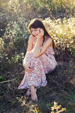 Çekici esmer kız çıplak ayakla oturur bahçe parkında çimenlerin üzerinde ayakkabı giymez, dışarıda sıcak vakit geçirir.