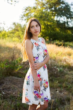 Yeşil bahçe parkında poz veren güzel, beyaz çiçekli bir elbise giymiş genç bir kadın.