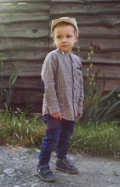 2-3 yaşlarında şık bir çocuk. Kırsal ahşap çitte arka planda. Kovboy kıyafetleri içinde yürüyor.