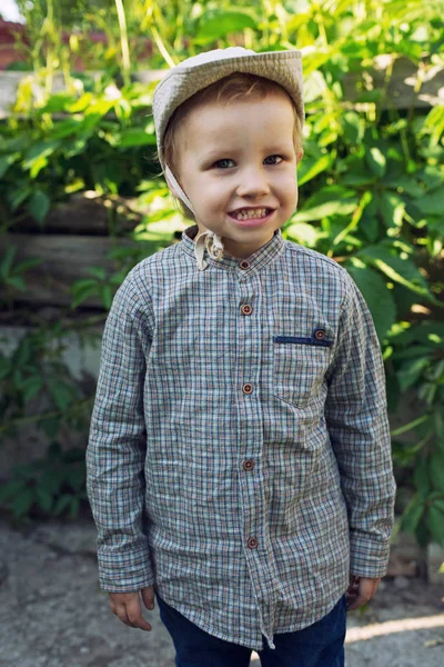 격자무늬 셔츠를 아이의 귀여운 바깥에 울타리가 배경에서 미소를 장난기많은 아이를 — 스톡 사진