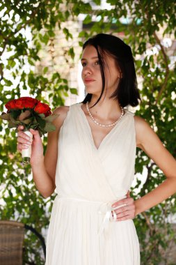 Genç, güzel, esmer gelin kısa düz saçlar ve küçük kırmızı güllerle poz veriyor.