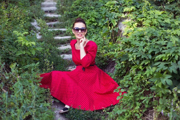 快乐而美丽的中年女性 身穿复古的红色迷你裙 头戴墨镜 头戴发夹 面容端庄 坐在楼梯上 — 图库照片