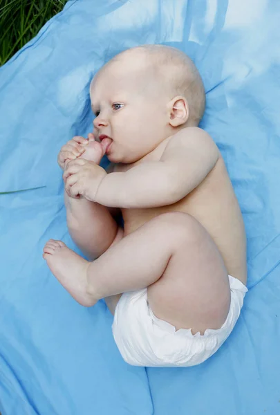 幼儿把脚趾放进嘴里 与脚玩耍 穿着白色的尿布 幼儿躺在室外 高瞻远瞩 — 图库照片