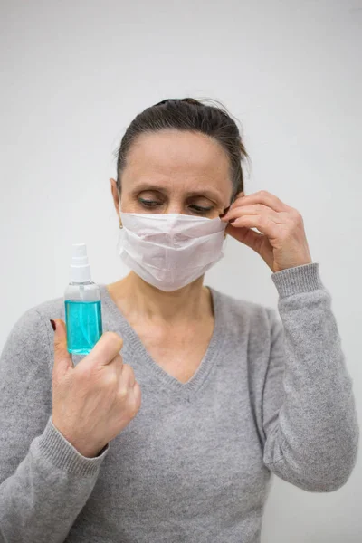 Woman hold blue sanitizer spray and fix face mask to protect from corona virusm world epidemia concept