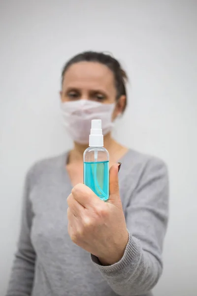 Woman in white mask hold blue sanitizer spray, focus on bottle, against world corona virus, white isolated background