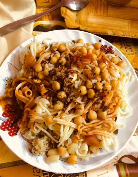 Mısır geleneksel yemeği Kosheri (Kushari, Koshari) beyaz tabakta kaşıkla, vejetaryen ucuz baharatlı, cheakpeas, mercimek, vermicelli, makarna, pirinç, domates sosu ve un soğanla kızartılmış baharatlı yemekler. 