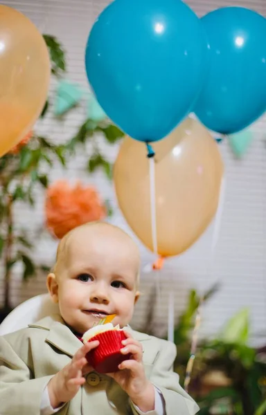 快乐的男婴在餐椅边吃着奶油生日蛋糕 带着气球微笑的小孩在家里聚会 — 图库照片