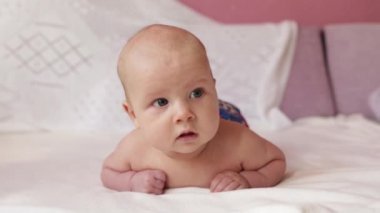 Bir kaç aylık küçük bebek karnında çıplak yatıyor, boynunu ve başını tutmak için alıştırma yapıyor.