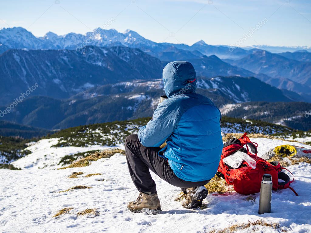 Mountaineer squatting at the top of the Peca mountain enjoying the view, Slovenia